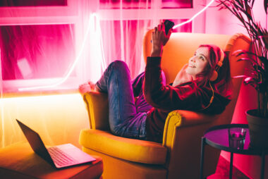 Jeune femme dans une chambre éclairée avec un néon rose et son téléphone qu'elle a personnalisé